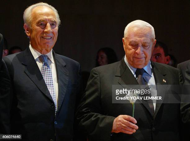 Israeli Prime Minister Ariel Sharon gazes at his white rose as he poses next to former premier Shimon Peres during the second and last day of...