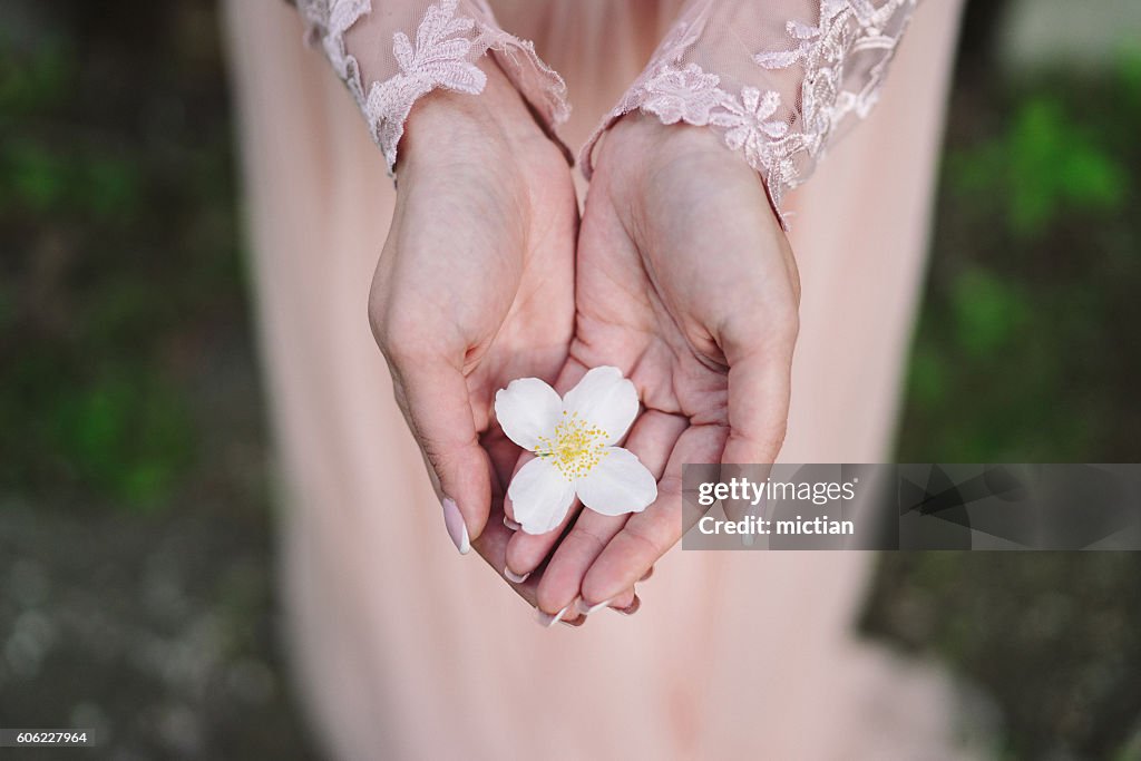 Jovem mulher caucasiana em vestido rosa segura uma flor de jasmim