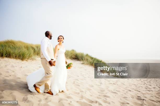 newlywed couple walking on beach - beach wedding fotografías e imágenes de stock