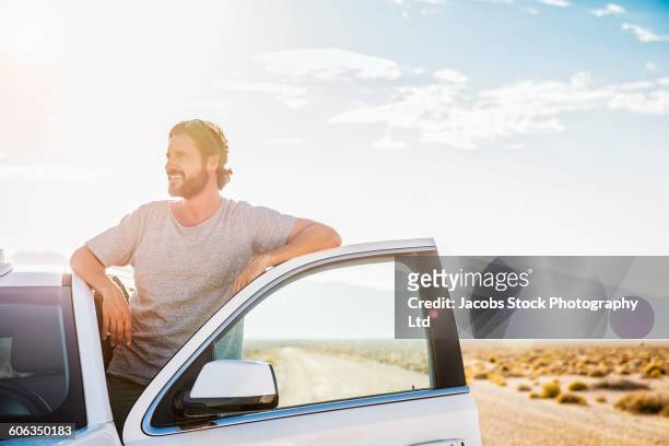 hispanic man standing in car on remote road - leaning stockfoto's en -beelden