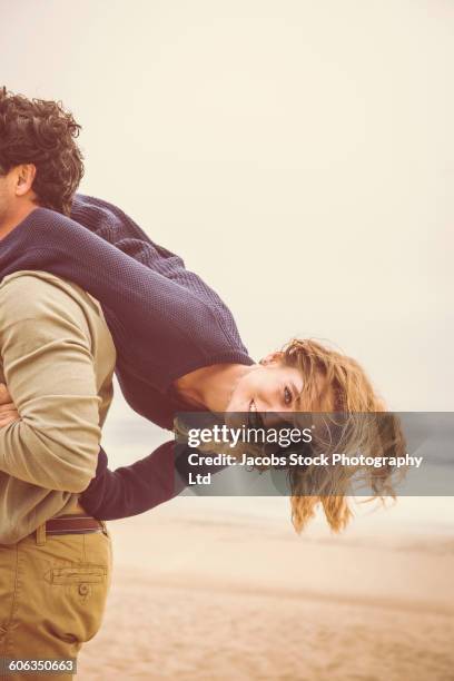 hispanic man carrying girlfriend on beach - holding upside down stock pictures, royalty-free photos & images
