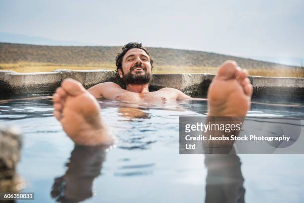 hispanic man laying in pool - bain à remous photos et images de collection