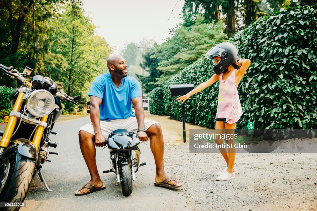 Father sitting on miniature motorcycle near daughter