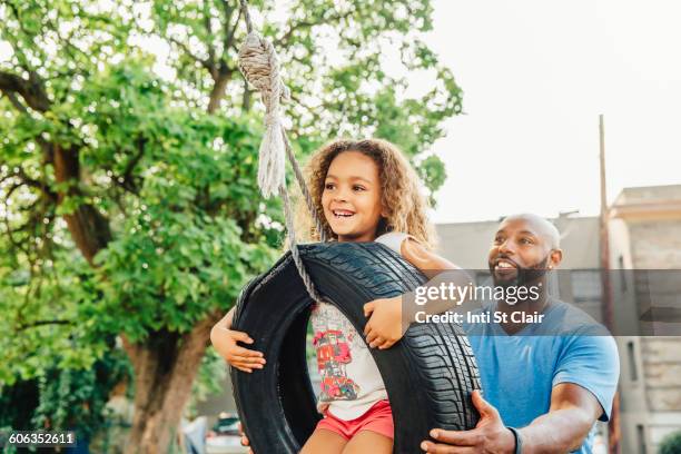 father pushing daughter on tire swing - autoreifen natur stock-fotos und bilder