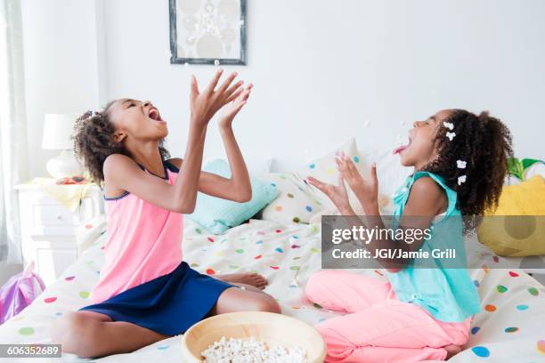 mixed race sisters eating popcorn on bed - catching food stock pictures, royalty-free photos & images