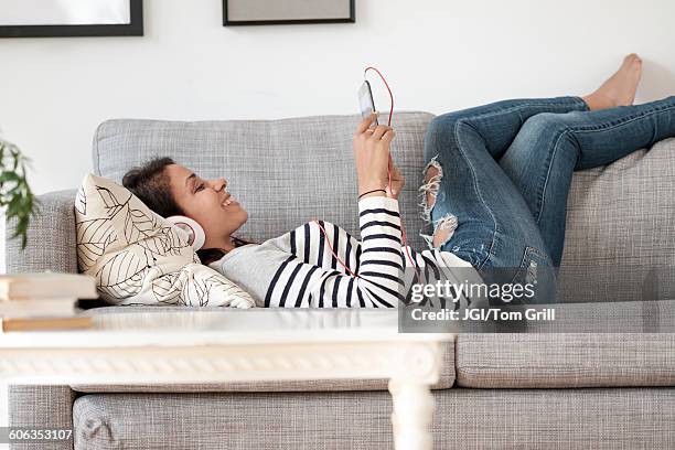 mixed race woman listening to headphones on sofa - zurücklehnen stock-fotos und bilder