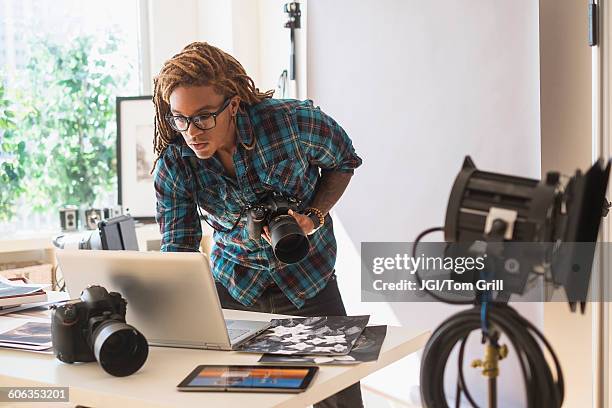 mixed race photographer using laptop in studio - équipement photographique photos et images de collection