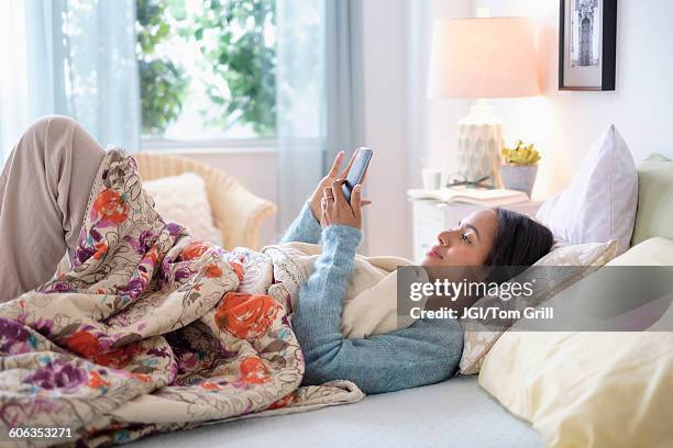 mixed race woman using cell phone in bed - awake day stockfoto's en -beelden