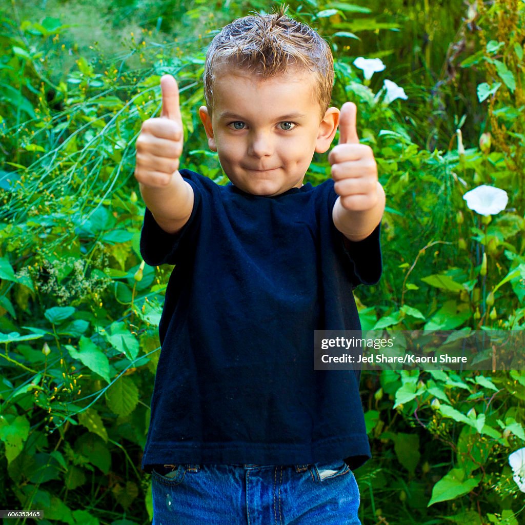 Caucasian boy giving thumbs up in garden