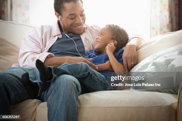 mixed race father and son listening to earbuds on sofa - child listening differential focus stock pictures, royalty-free photos & images