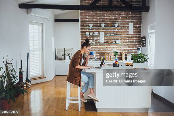 caucasian woman using laptop in kitchen - woman kitchen stock-fotos und bilder