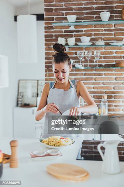 caucasian woman pouring sauce on pasta in kitchen - cooking apron stock pictures, royalty-free photos & images