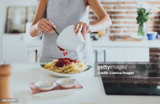 caucasian woman pouring sauce on pasta in kitchen - sauce stock pictures, royalty-free photos & images