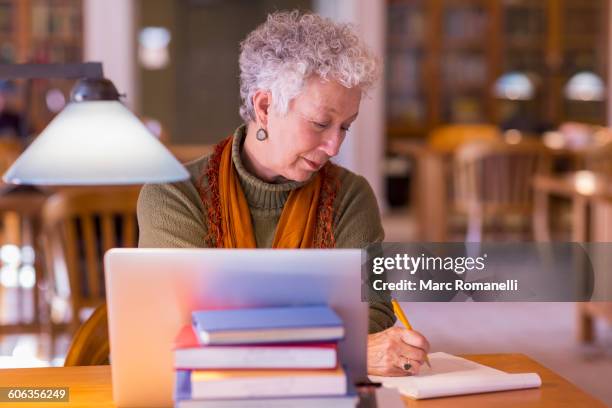 older mixed race woman using laptop in library - mature student stock pictures, royalty-free photos & images