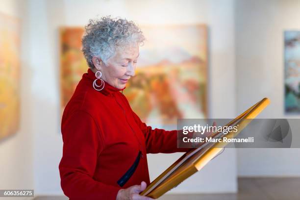 older mixed race woman holding picture in art gallery - art gallery owner stock pictures, royalty-free photos & images