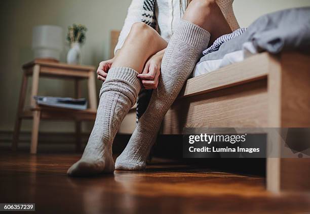 caucasian woman sitting on bed pulling up socks - chaussette photos et images de collection