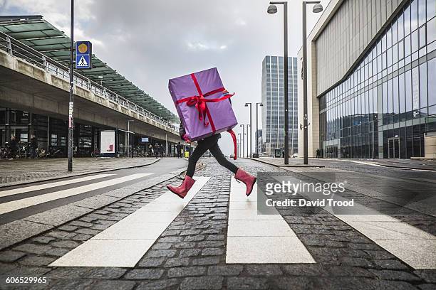 young girl running with large gift on street - christmas gifts stock pictures, royalty-free photos & images