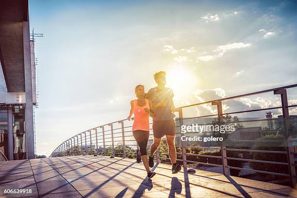 frau und mann joggen bei sonnenuntergang gemeinsam über berlinbrücke - jogging stock-fotos und bilder