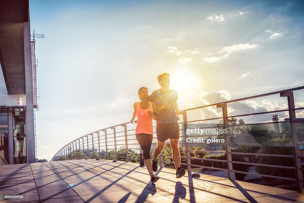 Woman and man jogging together over berlin bridge at sunset