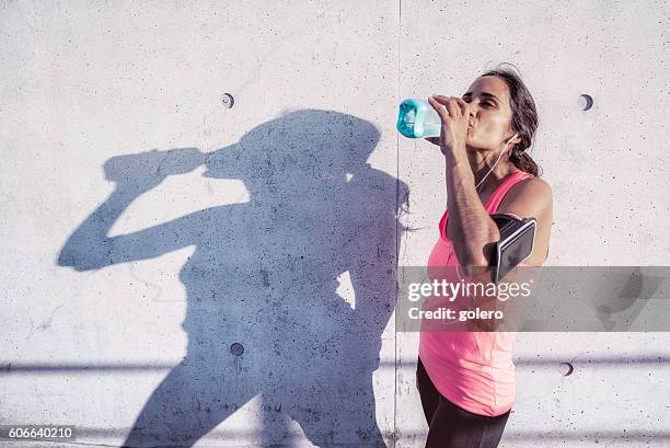 brazilian sportswoman drinking in front of concrete facade after running - urban areas　water front stockfoto's en -beelden