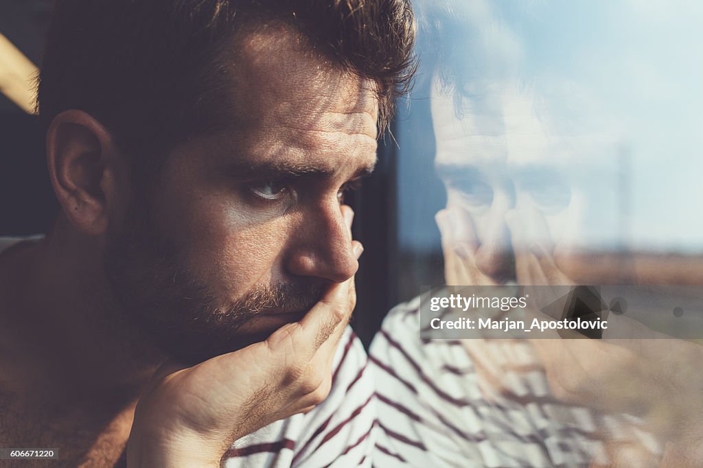 Sad young man looking through the window