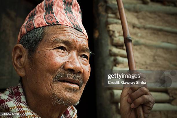 senior nepalese peasant man with stick near adobe house. - glimpses of daily life in nepal stock pictures, royalty-free photos & images