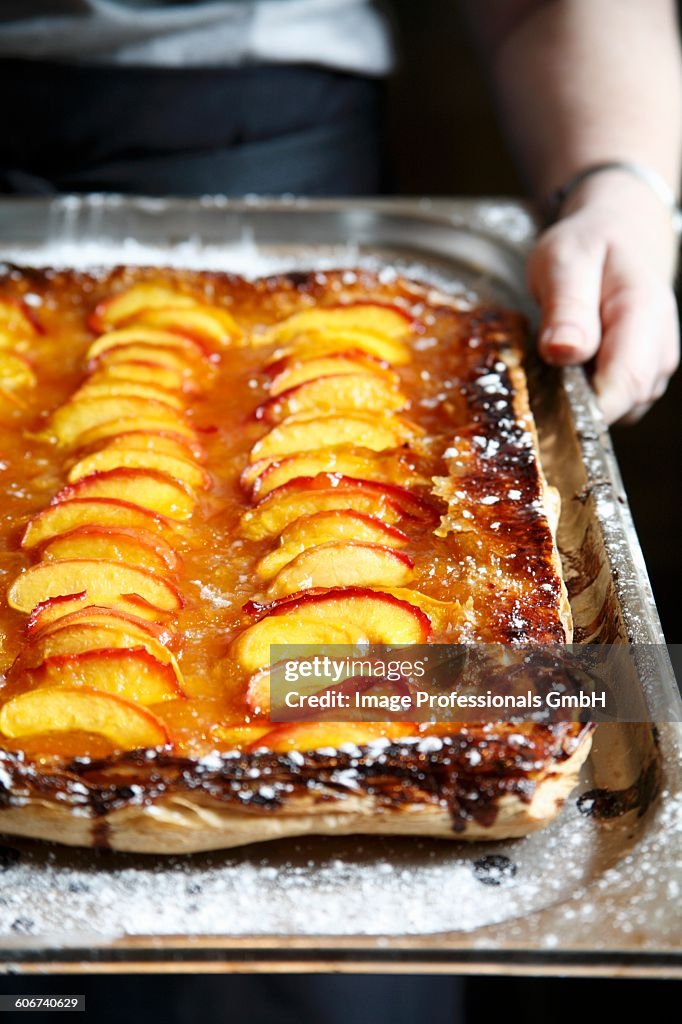 Hands holding a peach tart on a baking tray