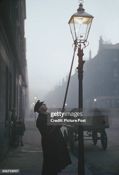 Lamplighter or 'leerie' lighting a gas lamp in a street in Glasgow, Scotland, 1955. The last remaining street gas lamp in Glasgow was ceremonially...