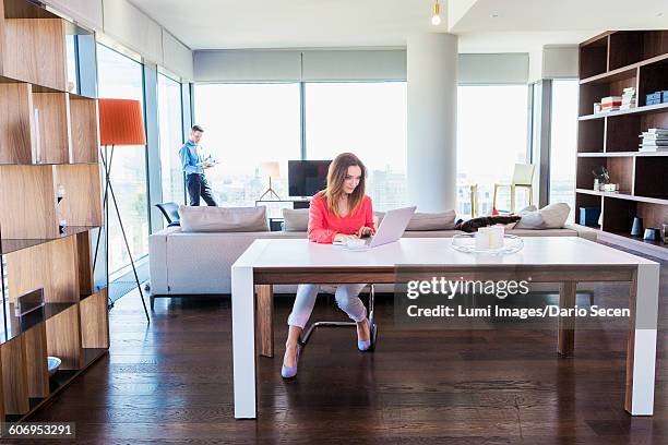 woman in apartment using laptop with man in background - dario secen stock-fotos und bilder