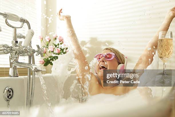 woman wearing headphones splashing in bath - woman in bathroom stockfoto's en -beelden