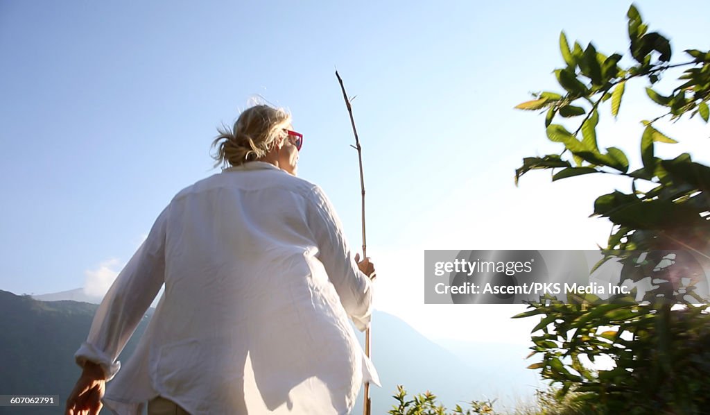 Woman hikes along mountain track, with bamboo pole