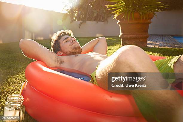 young man relaxing in pool - rode korte broek stockfoto's en -beelden