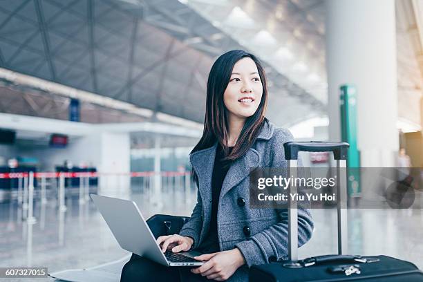 woman using laptop and looking away at airport - yiu yu hoi stockfoto's en -beelden