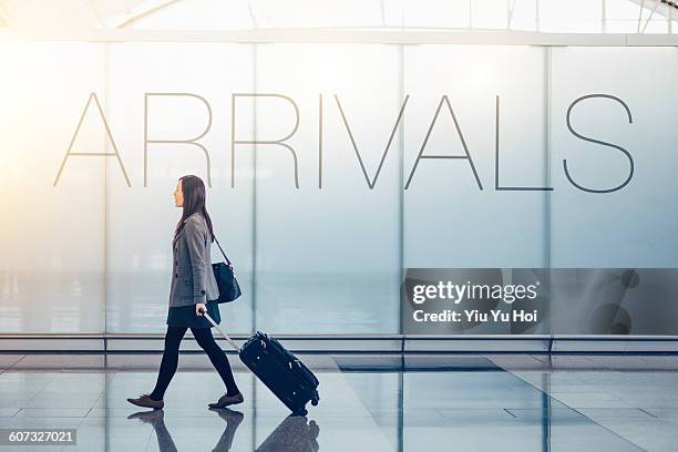 woman pulling suitcase in the airport arrival hall - arrivals foto e immagini stock