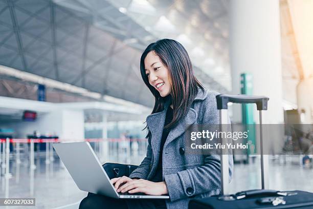 cheerful woman working on her laptop at airport. - yiu yu hoi stock pictures, royalty-free photos & images