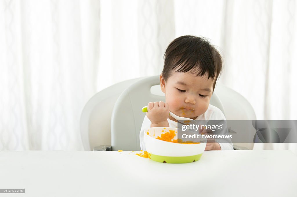 Asian toddler boy learning self feeding.