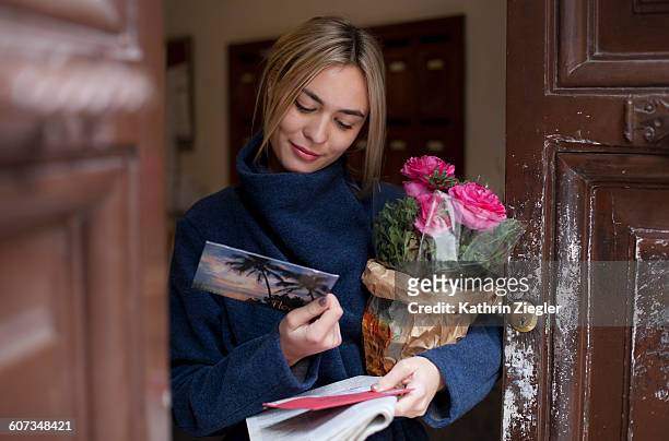 young woman reading postcard, holding flowers - ansichtskaart stockfoto's en -beelden
