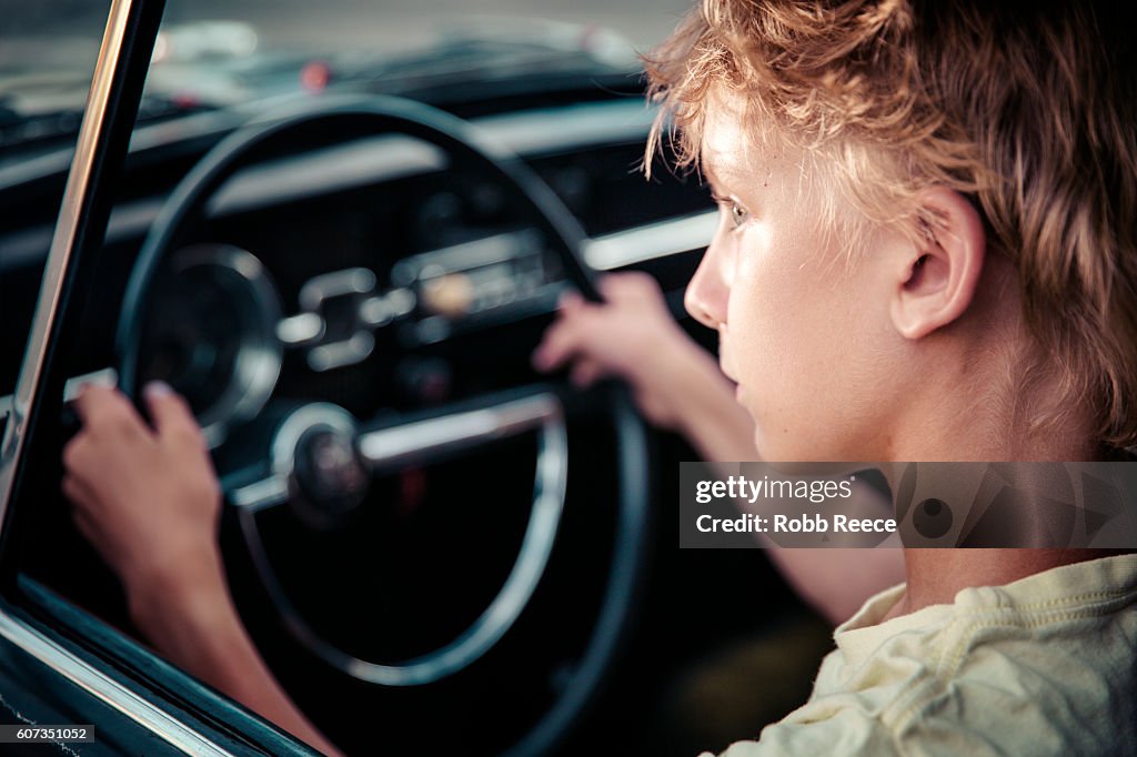 A young man sitting in the driver's seat of a vintage car