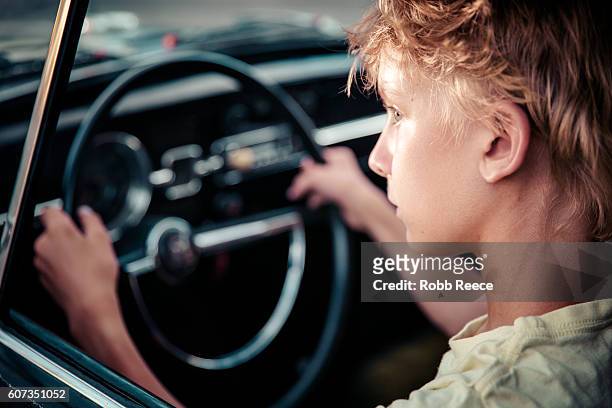 a young man sitting in the driver's seat of a vintage car - robb reece stock pictures, royalty-free photos & images