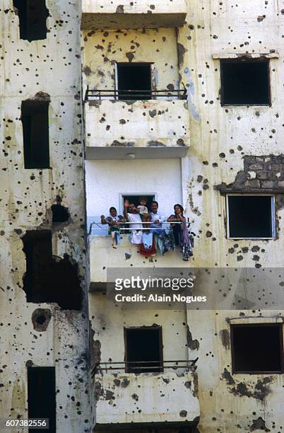 Lebanese family stands at the balcony of its flat, in a building marked by bullet holes.