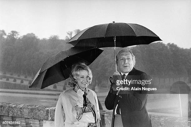 Actors Danielle Darrieux and Georges Wilson hold umbrellas on the set of the television show Les Jardins du Roi, or The King's Gardens. They are...