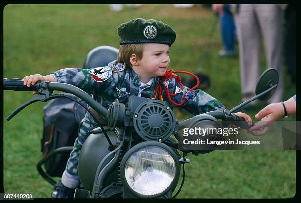 Young fan attending Normandy's World War II fighter plane air show mounts a vintage motorbike, decked out in full military garb. | Location: Falaise,...