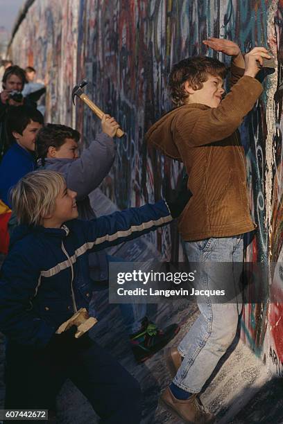 Kids holding hammers and bits of stone participate in the destruction of the Berlin Wall between the Postdam Platz and the Brandenburg Gate.