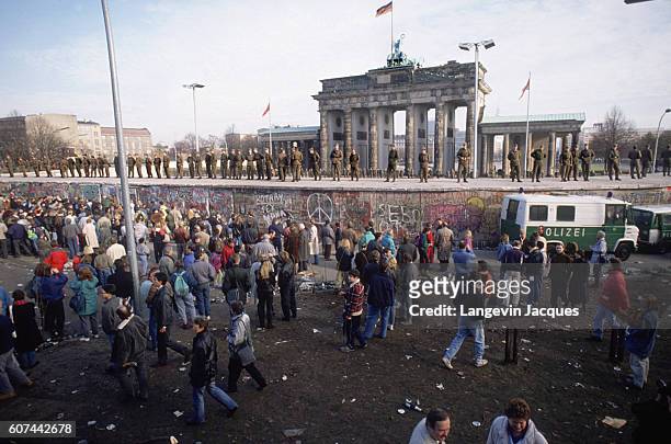 People gather on one side of the Berlin Wall, as German soldiers stand on a raised platform before the Brandenburg gate during the destruction of the...