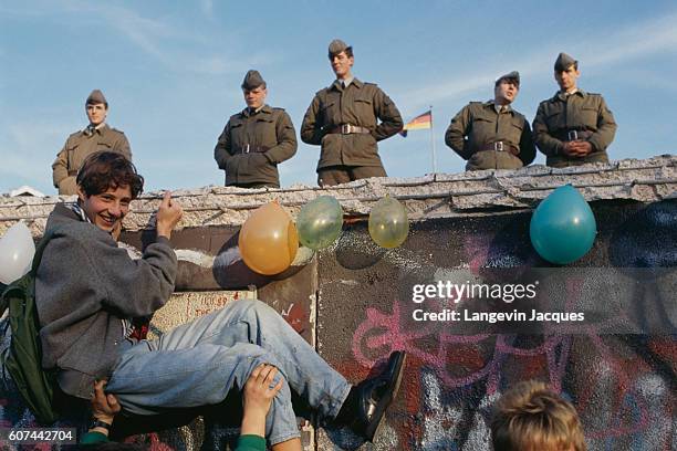 Young man is lifted at the edge of the Wall, as German soldiers look on, during the destruction of the Berlin Wall separating Postdam Platz from the...