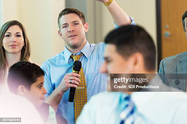 caucasian man raises hand during town hall meeting - government person stock pictures, royalty-free photos & images