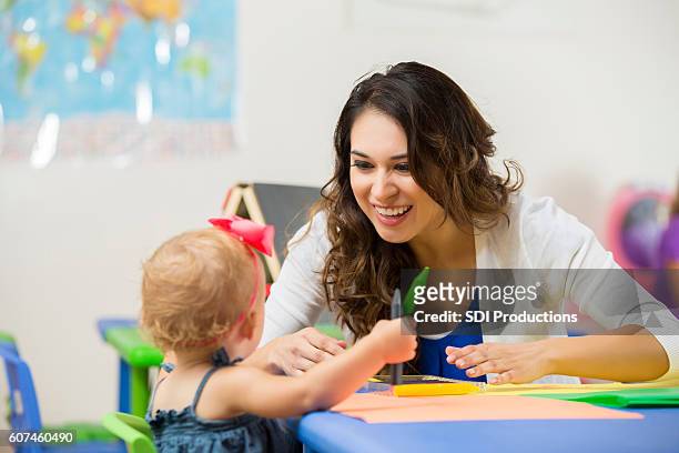 pretty daycare teacher helps toddler with coloring project - kindertijd stockfoto's en -beelden