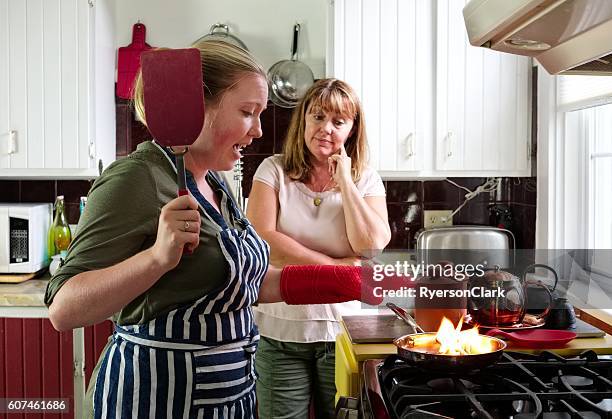 mother watches as daughter burns dinner, flaming frying pan. - burns supper stock pictures, royalty-free photos & images