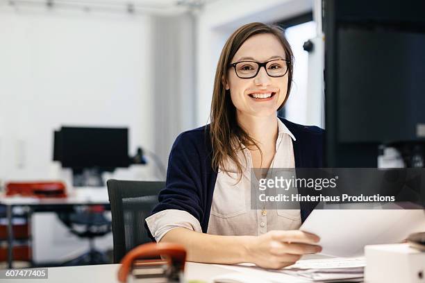 casual busineswoman smiling at a desk in an office - berufliche beschäftigung stock-fotos und bilder