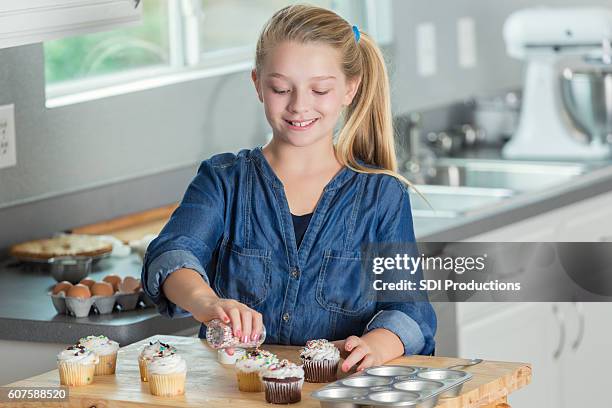 chica preadolescencia sonriente usando espolvoreados para decorar cupcakes - cupcakes girls fotografías e imágenes de stock